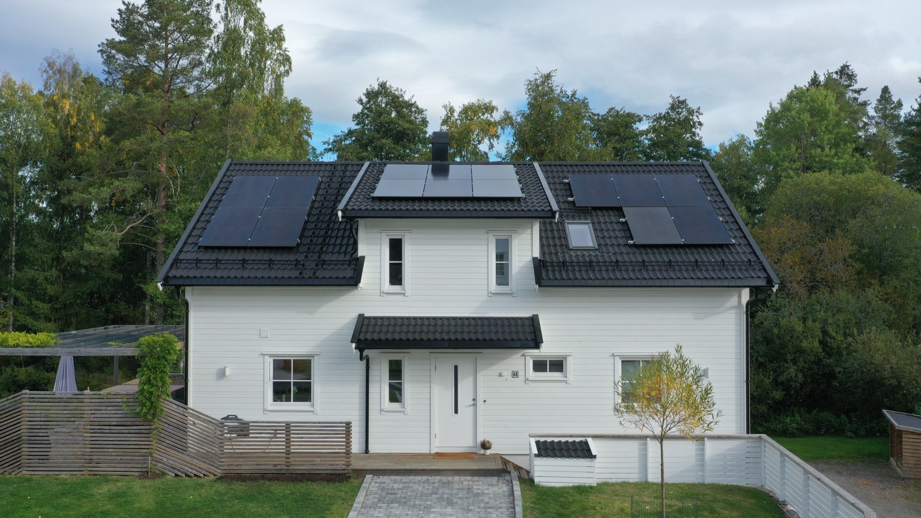 Norsk enebolig med solcellepaneler, treterrasse og grønn hage
